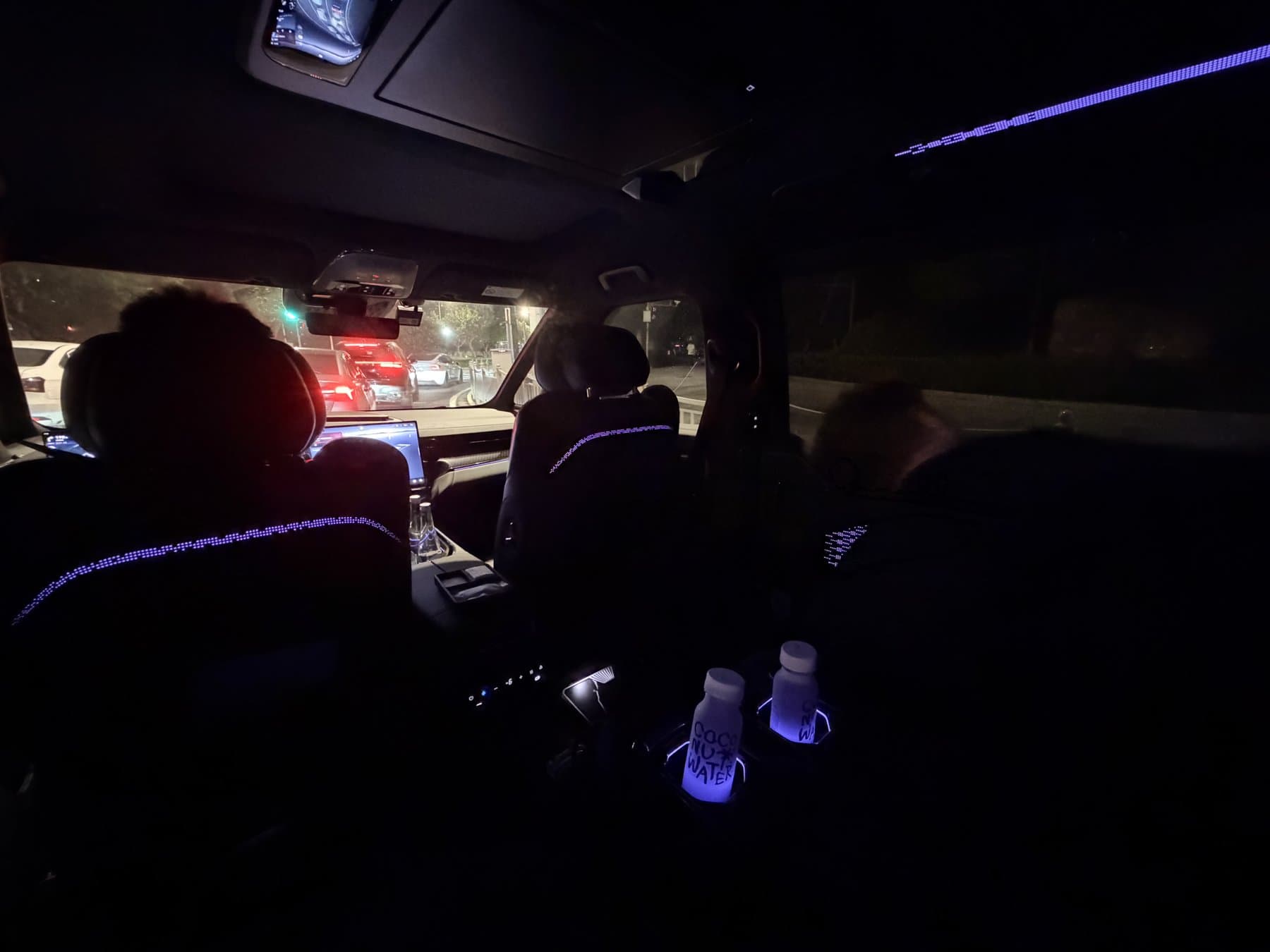 Dark back seat of a car in night traffic, dashboard lights visible ahead